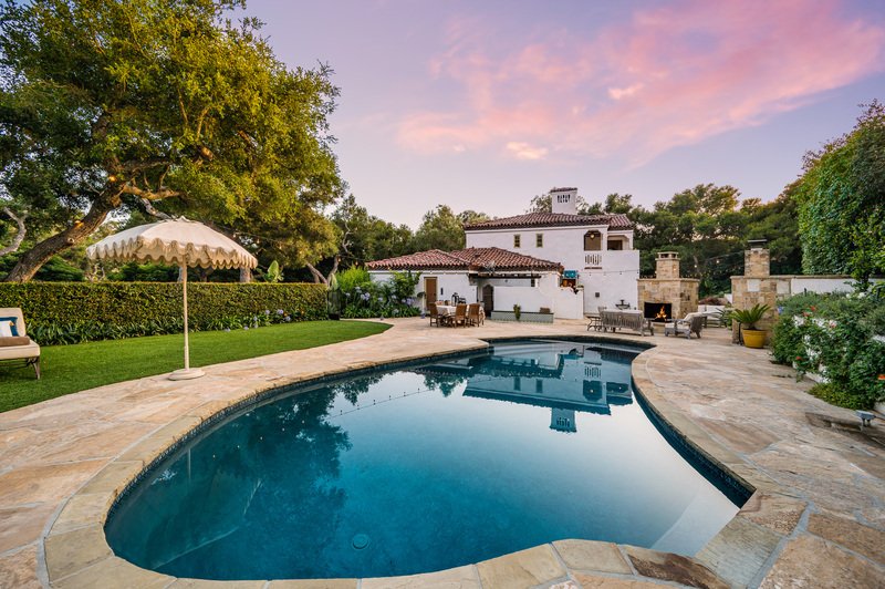 Casa residencial con alberca iluminada al atardecer, terraza de madera y área exterior ideal para convivencia.